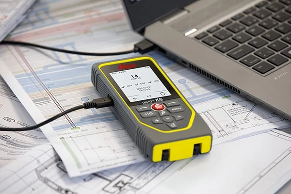 Leica DISTO X6 ob računalniku in načrtih, povezan s kablom USB